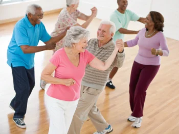 Un grupo de personas mayores disfrutando de una clase de baile en un centro comunitario, mostrando sonrisas y energía en un ambiente vibrante y acogedor.